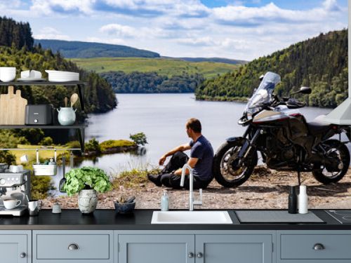 Adventure motorcycle and biker man traveling, sitting and watching landscape with lake and mountains, freedom travel lifestyle in Wales UK