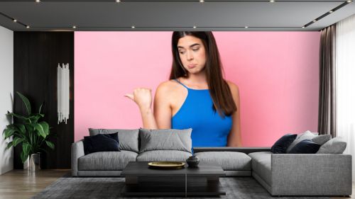 Young Brazilian woman isolated on pink background unhappy and pointing to the side