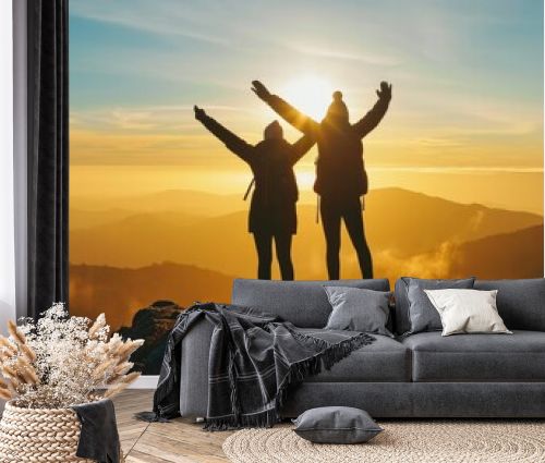 Two people silhouette with arms raised up on mountain top at sunset