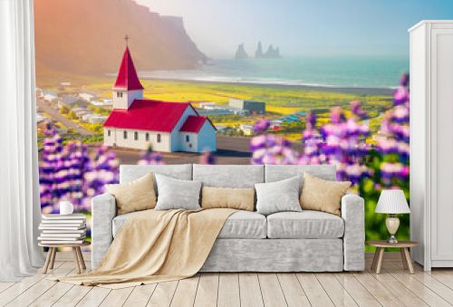 Wonderful morning view of Vikurkirkja (Vik i Myrdal Church) with Reynisdrangar on background, Vik location. Stunning summer scene of Iceland with field of blooming lupine flowers. Travel to Iceland.