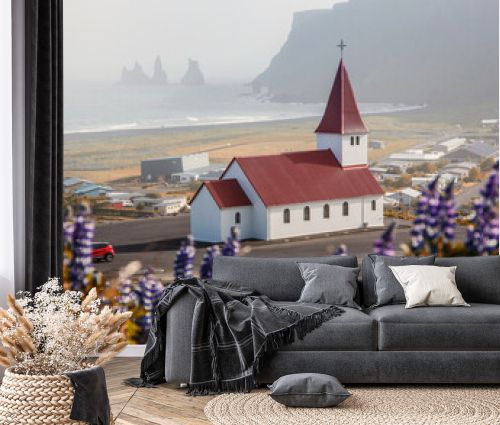 Incredible view of Vikurkirkja christian church and field of blooming lupine flowers on foreground in sunny day. Vik village is a one famous natural landmark and travel destination plase of Iceland